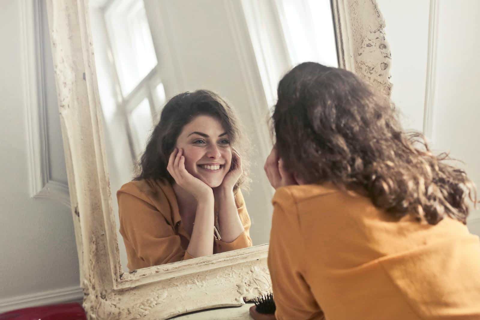 Sun signs, astrology, A cheerful woman smiles at her reflection in a vintage-style mirror, exuding positivity and warmth.
