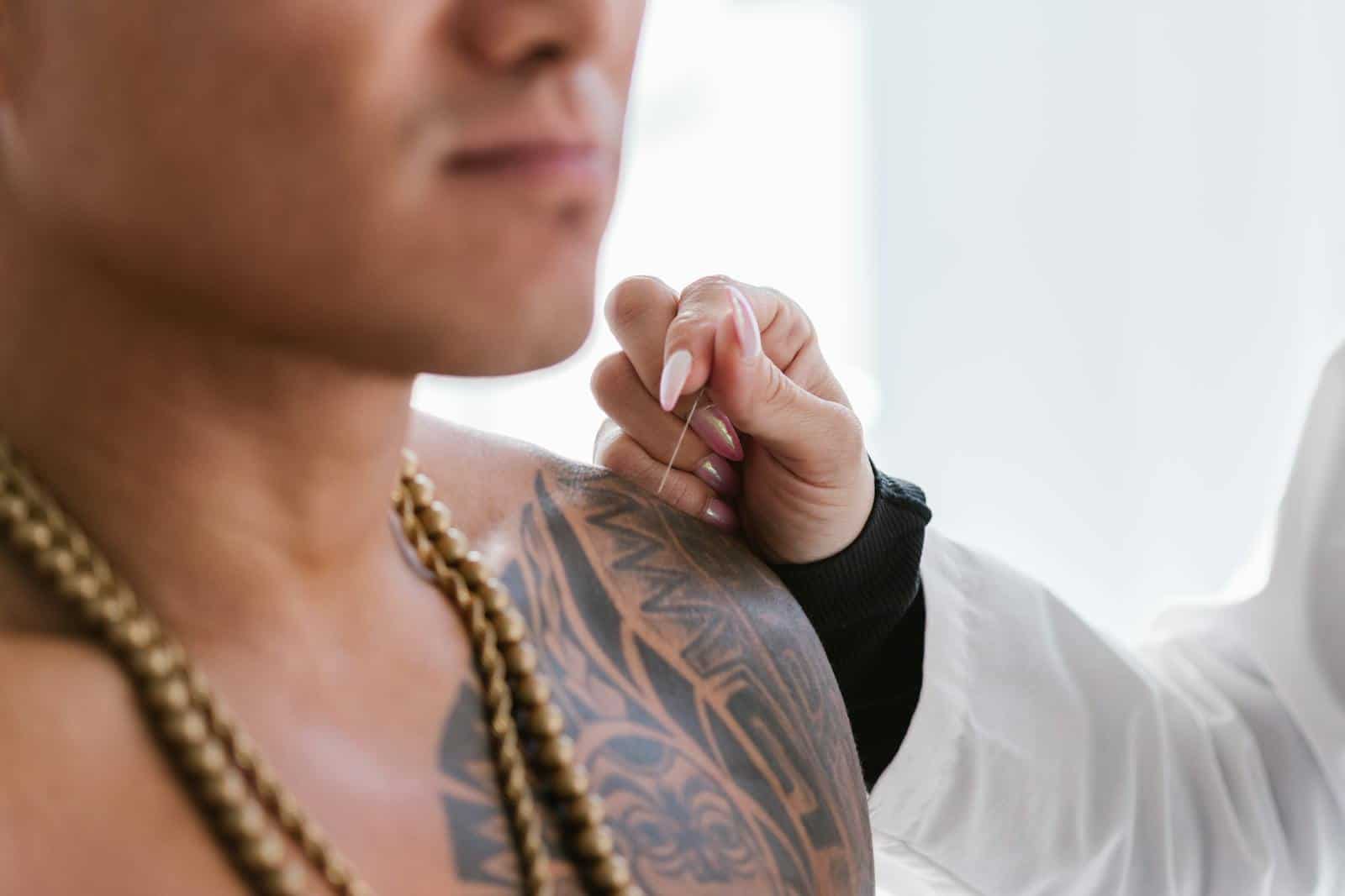 Unlocking the Power of Traditional Chinese Medicine, Close-up of tattooed man's shoulder, receiving acupuncture treatment by a practitioner.