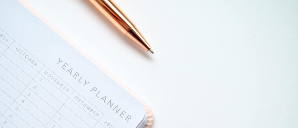 A stylish yearly planner open to a 2020 calendar page, accompanied by a golden pen on a clean white surface.
