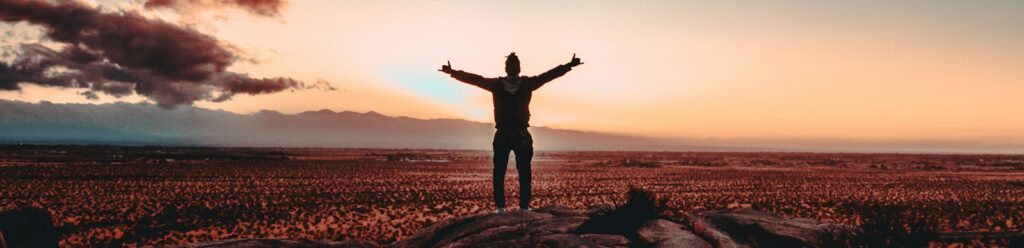 person standing on rock raising both hands