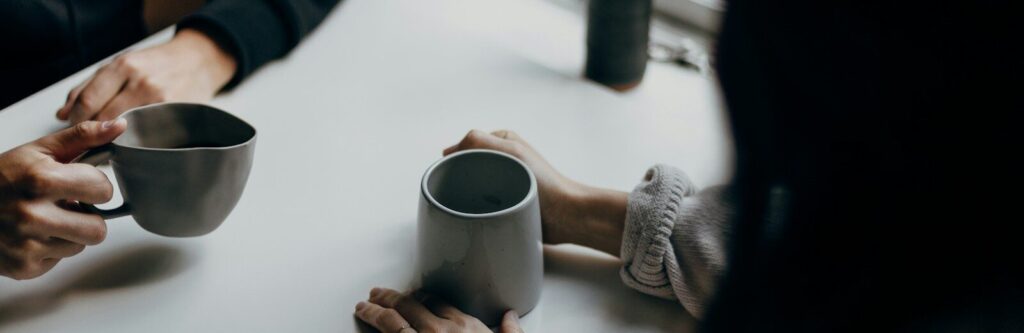 two people holding gray mugs at table